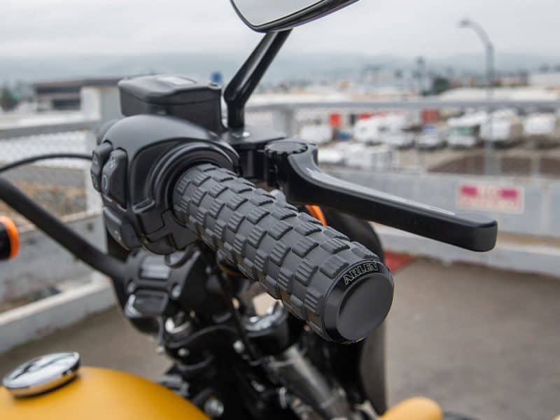 Black motorcycle handlebar with textured grip and control switch, riding gear features, close-up view.