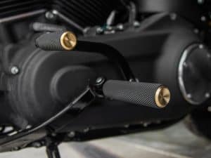 Stylish motorcycle foot pegs with textured black metal and gold accents for enhanced grip and aesthetics.