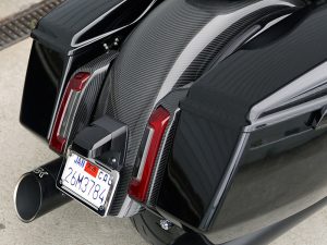 Steel-adorned Harley motorcycle with sleek black and carbon fibre finish, classic tail lights and custom exhaust.