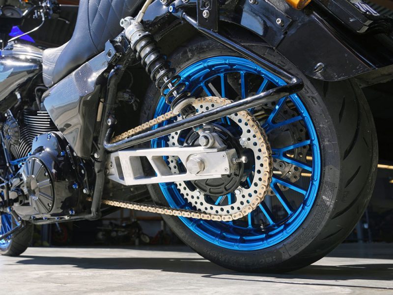 High-performance motorcycle rear wheel with blue rim and custom chain drive.