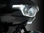 Modern black motorcycle headlight with LED daytime running lights.