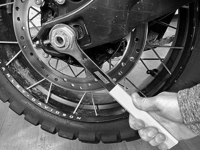 High-performance motorcycle wheel maintenance by Revelry Cycles, featuring professional tool for wheel adjustment.