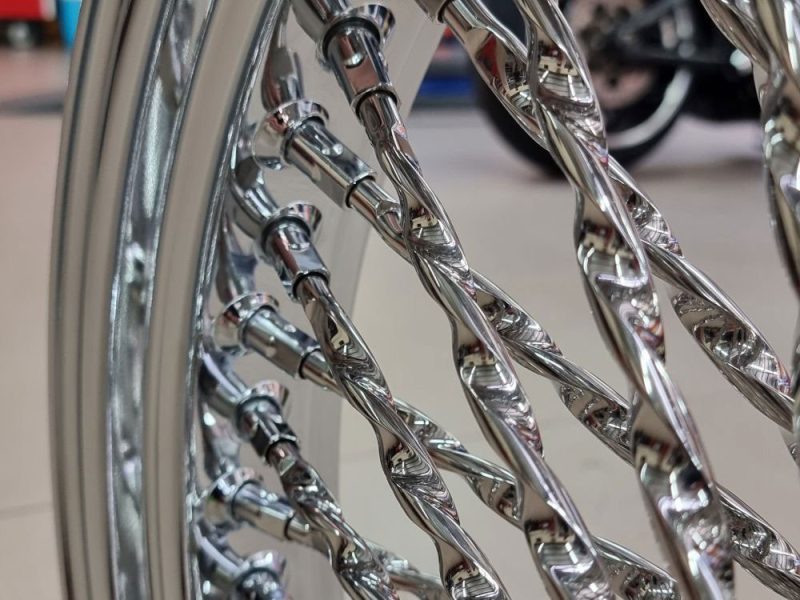 Shiny chrome motorcycle wheel with intricate twisted spokes, detailed close-up for Revelry Motorcycles SEO image.