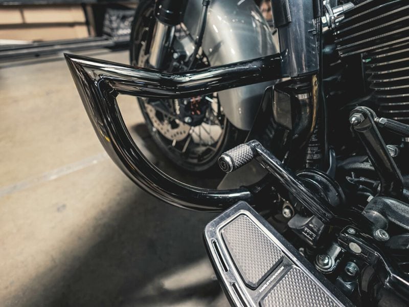 Sleek black motorcycle crash bar and footrest on a custom Harley Davidson at Revelry Motorcycles.