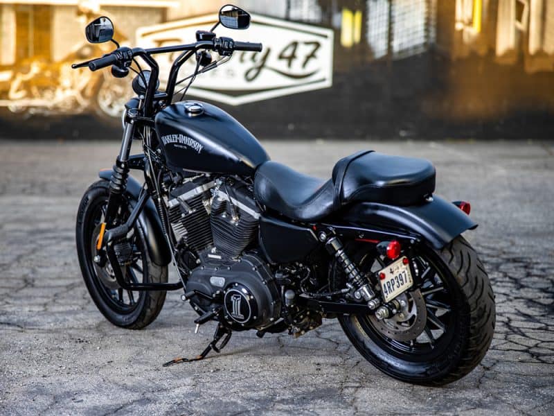 Harley Davidson black motorcycle parked on street in front of Revelry Cycles shop.