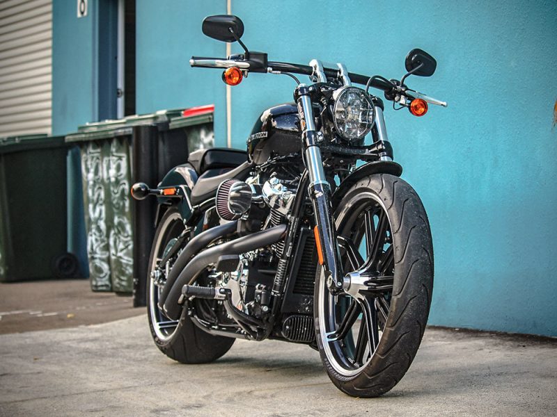 Vivid black Harley-Davidson motorcycle parked against a blue wall, showcasing classic cruiser style.
