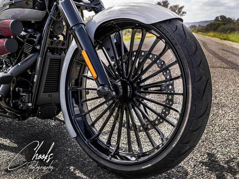 Black motorcycle front wheel with alloy spokes and disc brake on a rural road.
