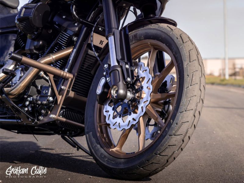 Brake disc and tire on black motorcycle with custom gold wheel at Revelry Motorcycles.
