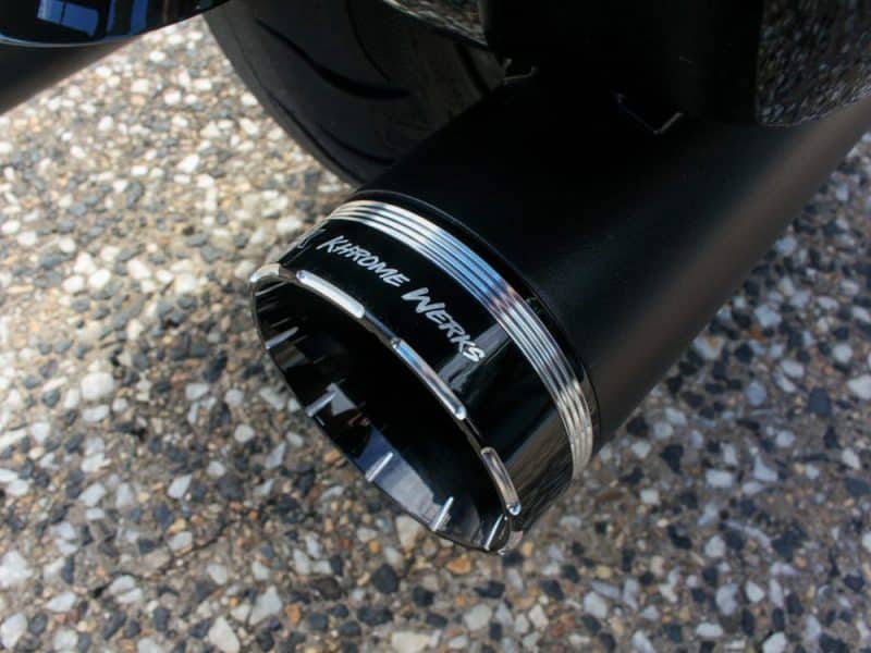 Chrome's Works motorcycle exhaust pipe close-up on gravel background.