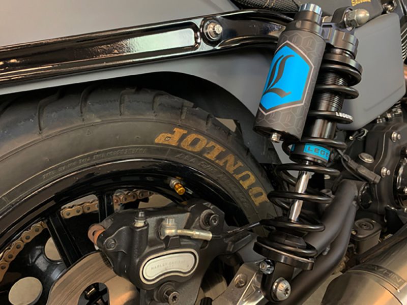 High-performance motorcycle rear wheel and suspension with Dunlop tyre and RevelryCycles branding.