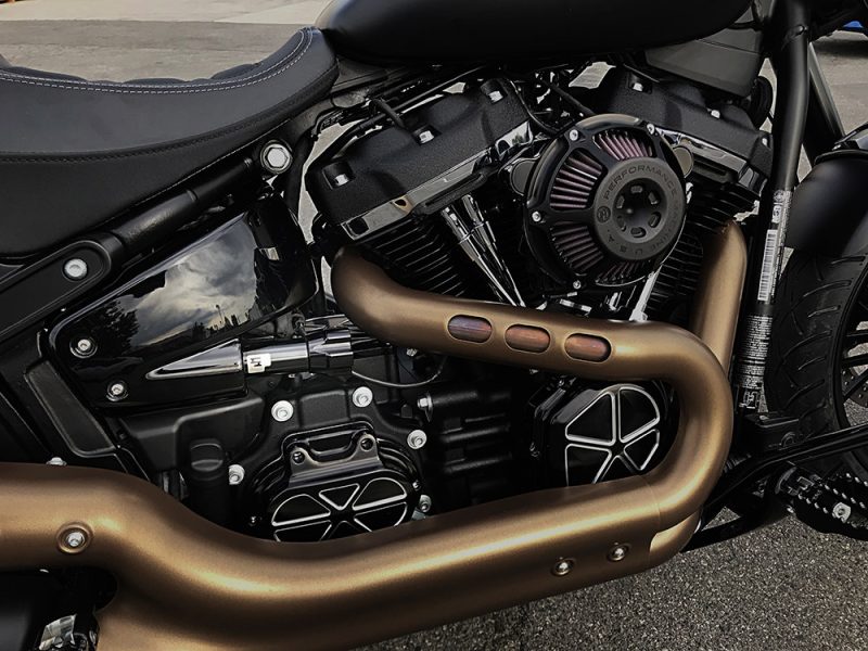 V-Twin motorcycle engine with custom exhaust pipes and performance air filter, sleek black and bronze design.