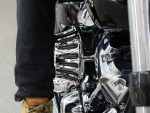 Shiny chrome motorcycle engine with a person's leg in black jeans and tan leather boot.