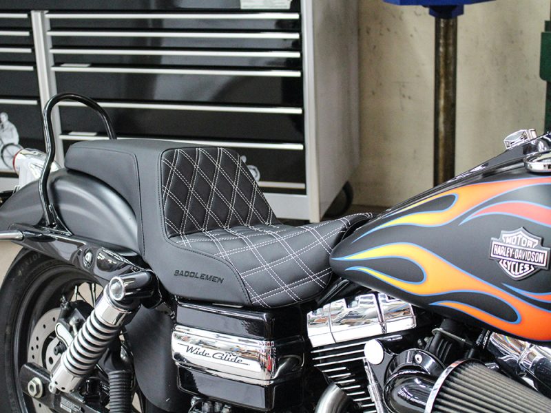 Black leather motorcycle seat with diamond stitching on Harley-Davidson bike in a workshop setting.