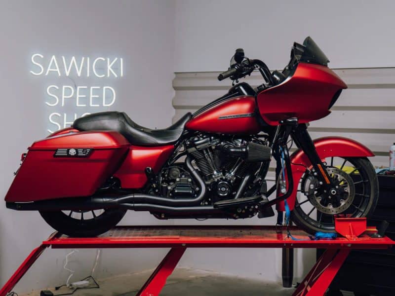 Vivid red American-style touring motorcycle on service lift for custom modifications.