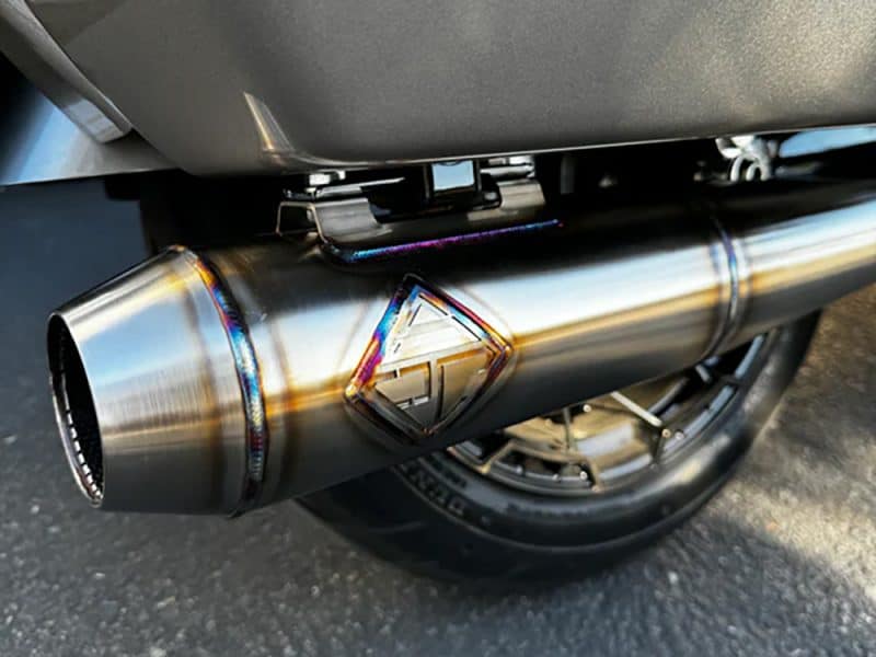 Shiny motorcycle exhaust pipe with colourful welds at Revelry Cycles, promoting high-performance motorcycle accessories.