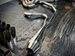 Sleek chrome motorcycle exhaust pipe on workbench at Revelry Motorcycles shop, upgrade your bike performance.