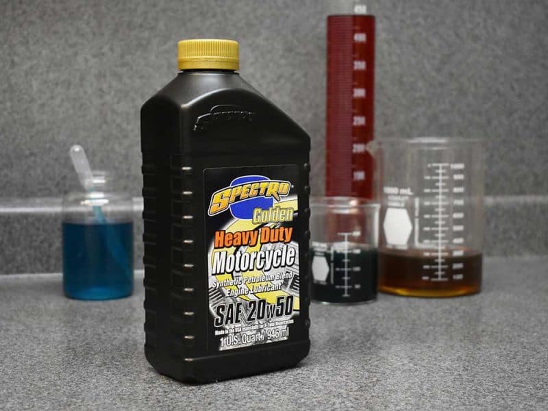 Synthetic motorcycle engine oil in a Revelry Motorcycles workspace, with laboratory beakers and measurement tools.