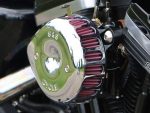 Chrome motorcycle engine component with purple air filters, reflecting outdoor scenery, branded S&S Cycle, high-performance parts for custom bikes.