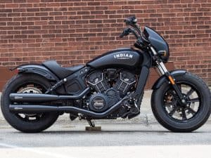 Bold black Indian Scout motorcycle parked on city street with brick wall background.