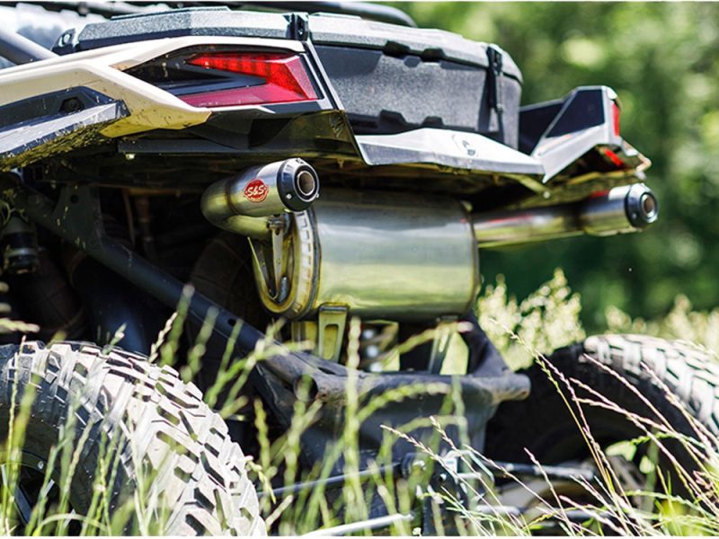 SAS off-road exhaust system on a quad bike or ATV in a grassy outdoor setting.