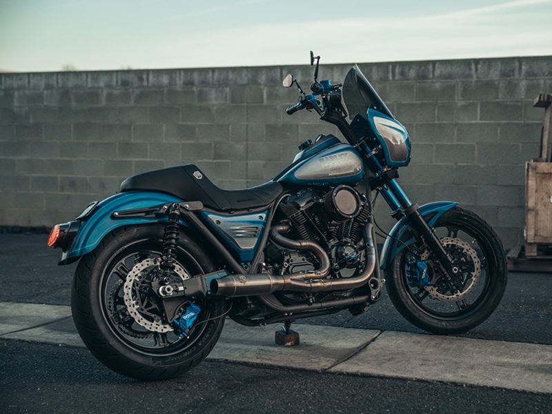 Vivid blue custom cruiser motorcycle parked on urban street, showcasing Revelry Motorcycles' craftsmanship and design.