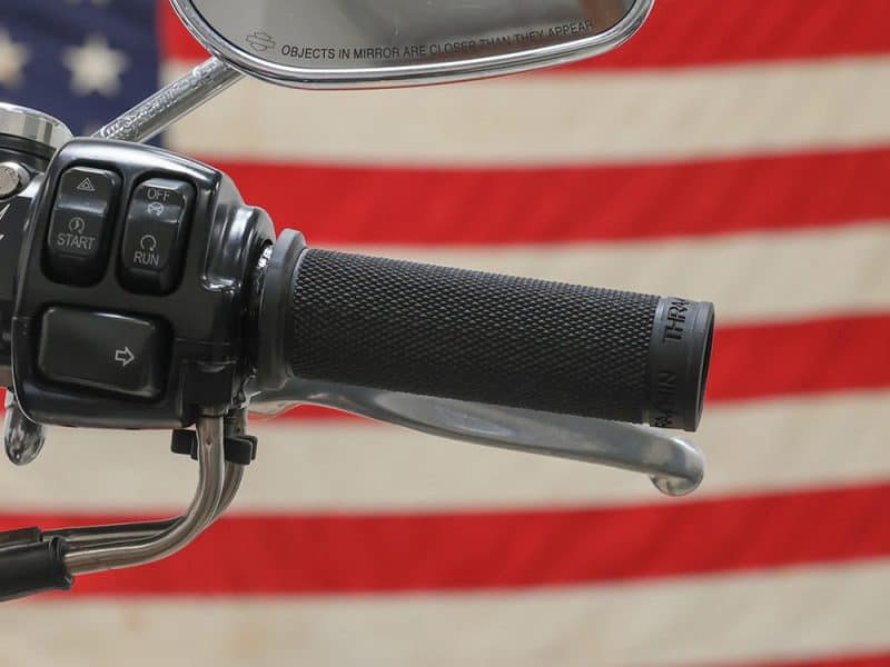 Handlebar grip and mirror close-up on a motorcycle with an American flag background.