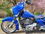 Blue custom motorcycle with chrome accents on a scenic spring background.