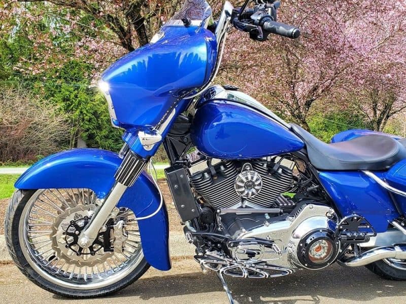 Blue custom motorcycle with chrome accents on a scenic spring background.